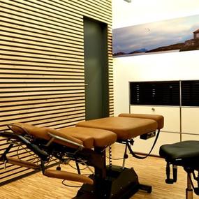 Moderne chiropraktische Praxis mit höhenverstellbarer Behandlungsliege und Holzdekor.